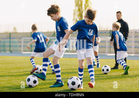 Children Training Soccer on Field. Young Kids Boys kicking Soccer Football Balls on Grass Pitch. Kids in Sportswear Practice Soccer Skills - Stock Photo